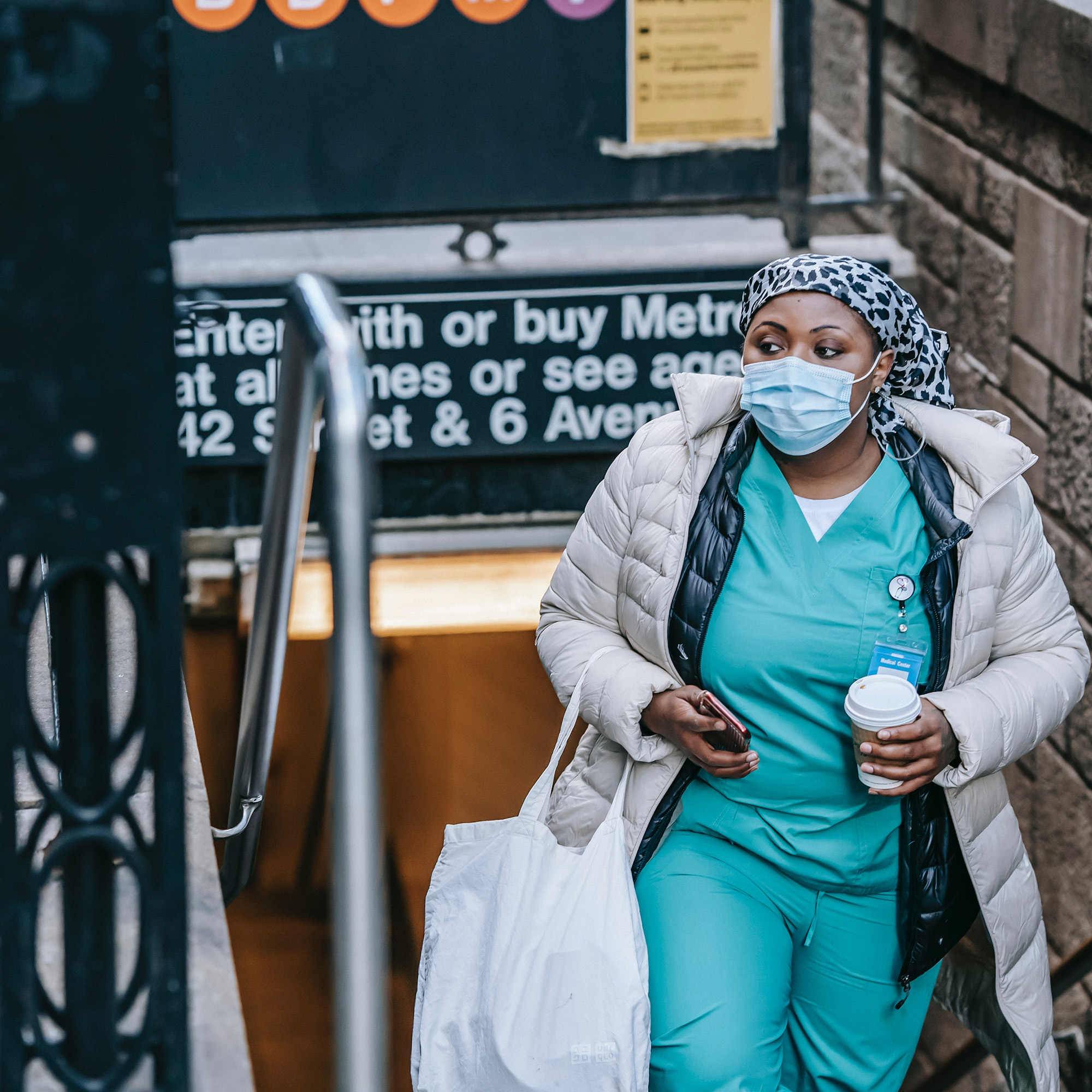 masked travel nurse leaving subway with coffee